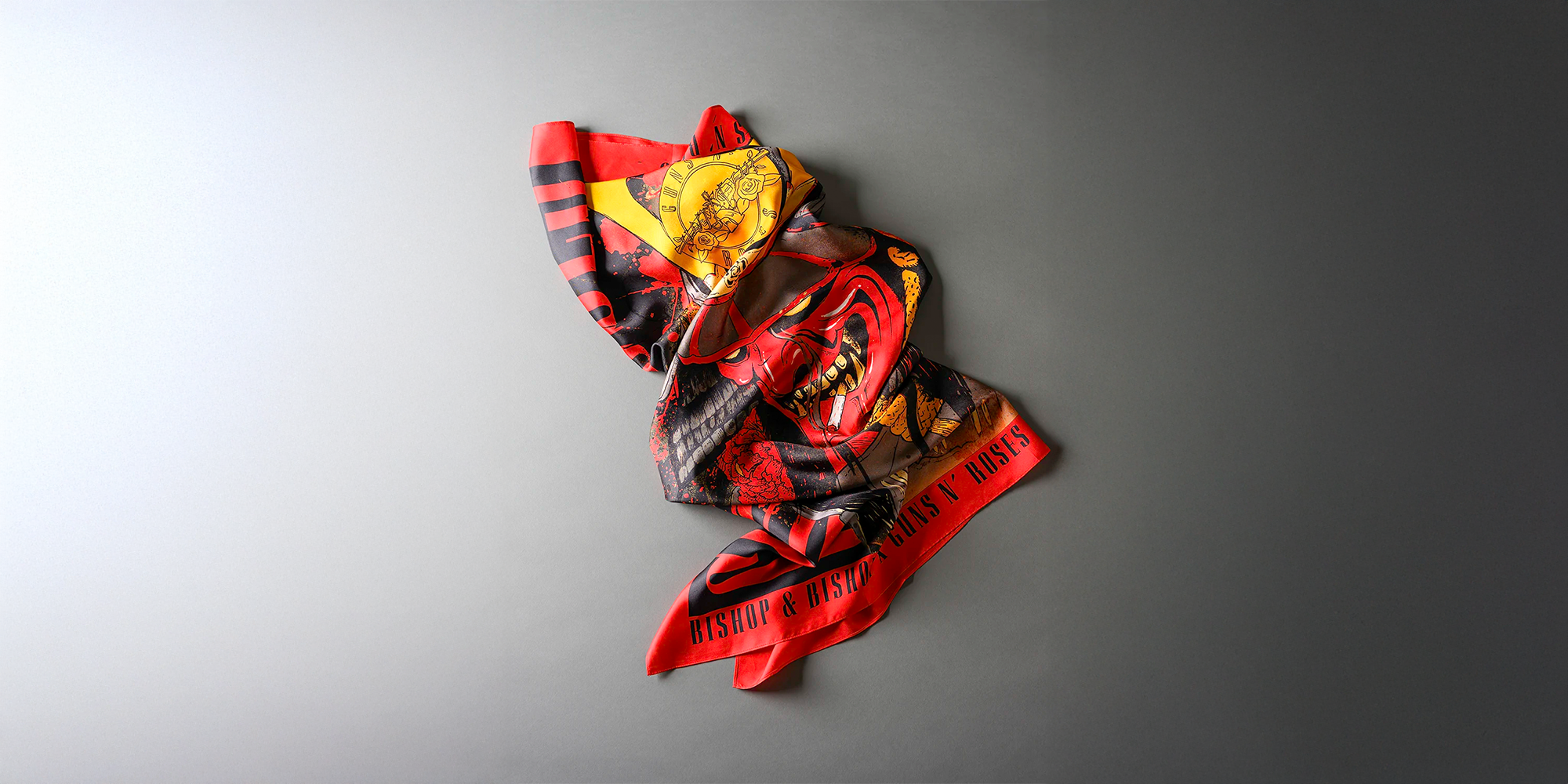 Red scarf featuring Bishop & Bishop and Guns N’ Roses graphic designs, displayed on a gray background.