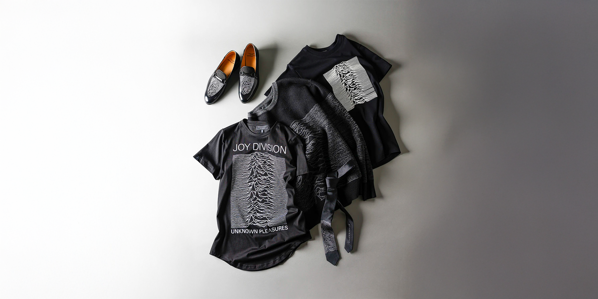 Black T-shirts and shoes with matching Joy Division graphic designs and text, displayed on a white surface.