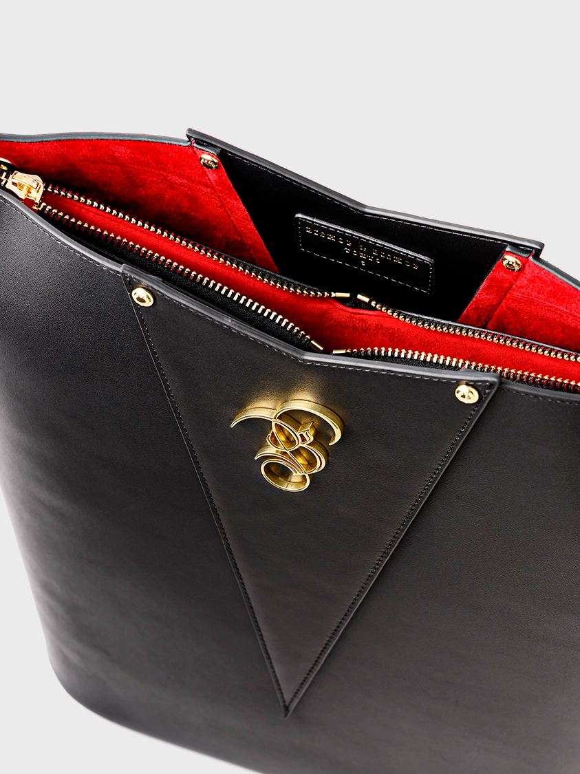 Black handbag with gold clasp and red interior on a gray background.