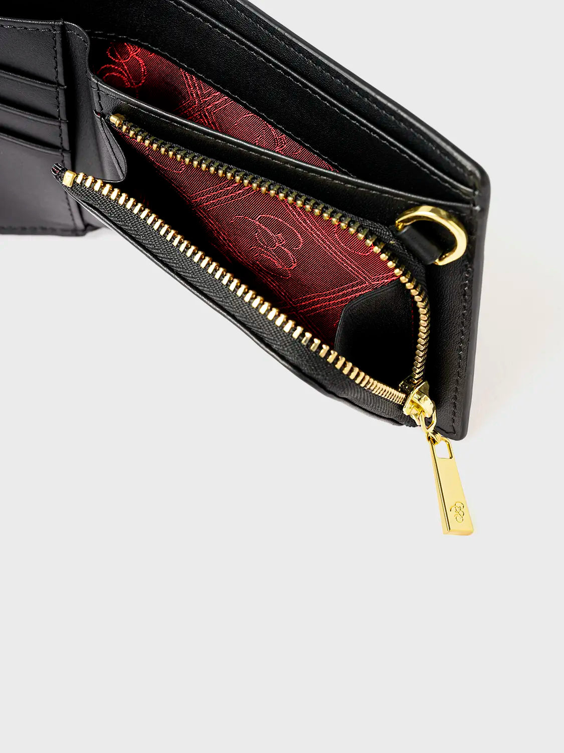 Close-up of a black wallet with a gold zipper, showing an open compartment and red interior lining with the Bishop & Bishop logo.