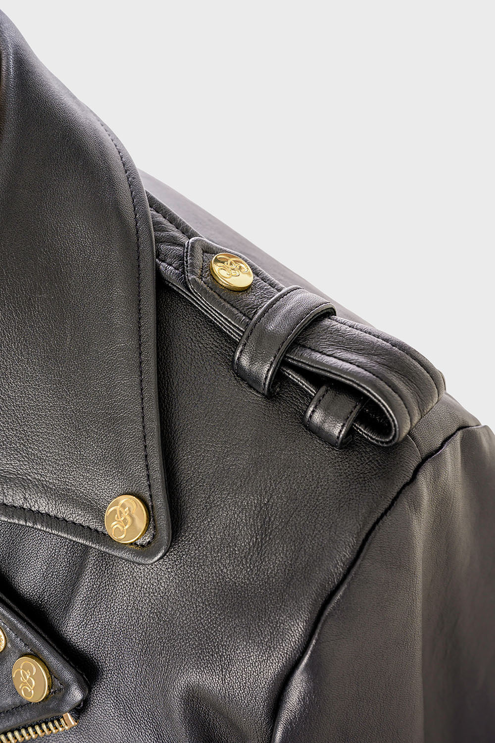 Close-up of the shoulder strap of a black leather jacket, showing a button engraved with the “Bishop & Bishop” logo.