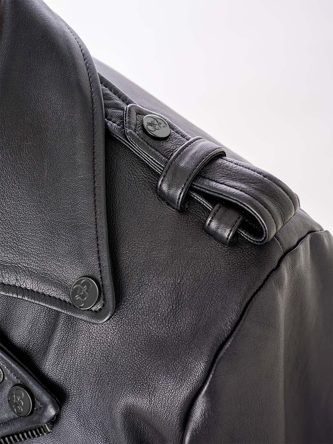 Close-up of the shoulder strap of a black leather jacket, showing a button engraved with the “Bishop & Bishop” logo.