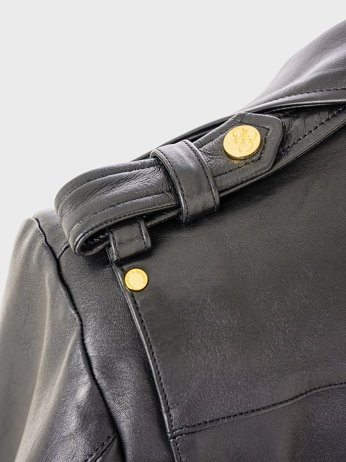 Close-up of the shoulder strap of a black leather jacket, showing a button engraved with the “Bishop & Bishop” logo.