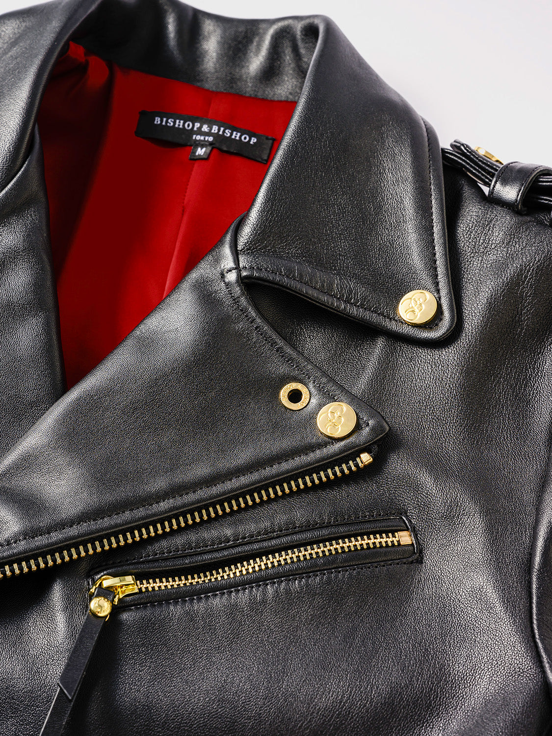 Close-up of the front collar of a black leather jacket, showing buttons engraved with the “Bishop & Bishop” logo and red interior lining.