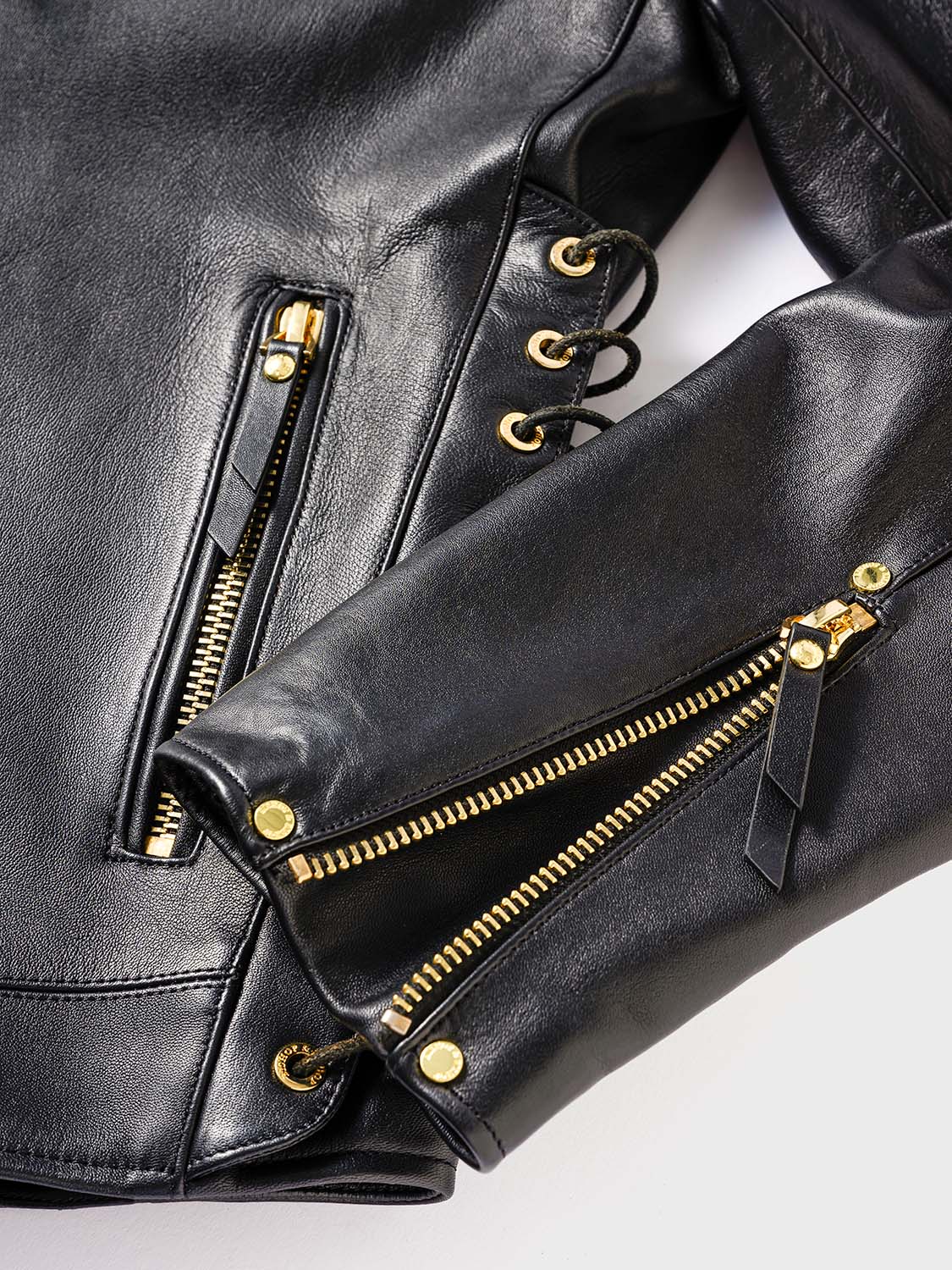 Close-up of the sleeve of a black leather jacket featuring a gold zipper.