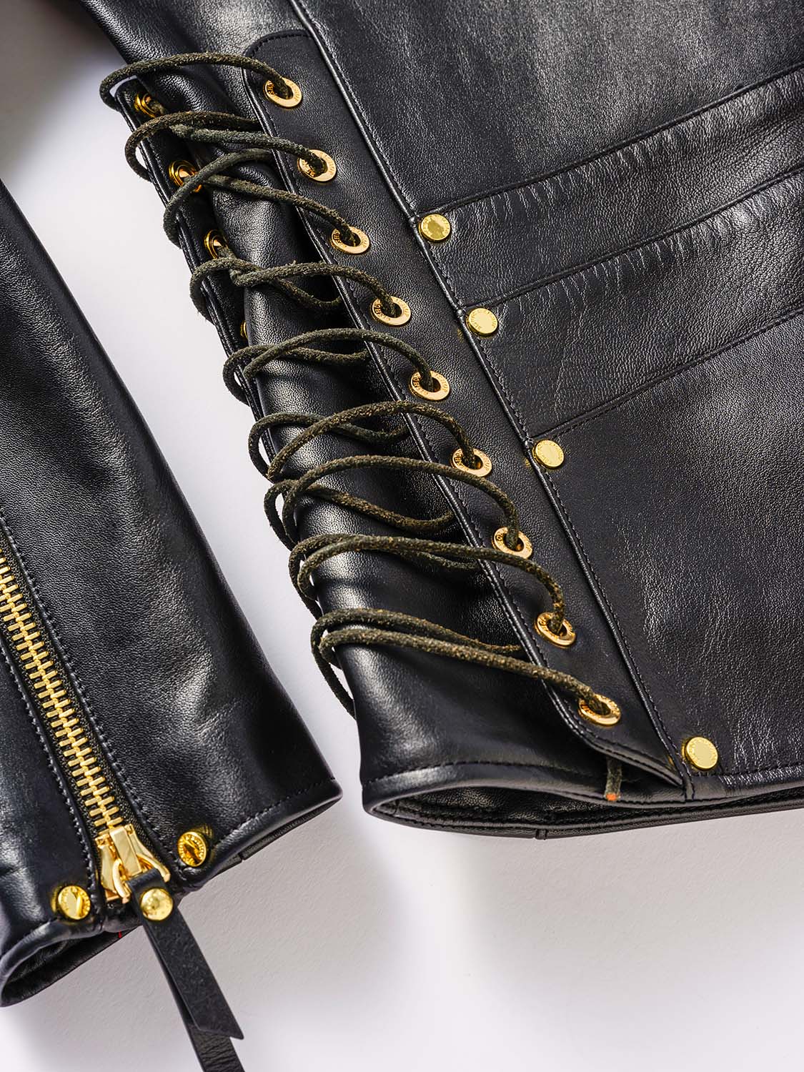 Close-up of the side of a black leather jacket featuring lace-up detailing with cord threaded through metal eyelets.