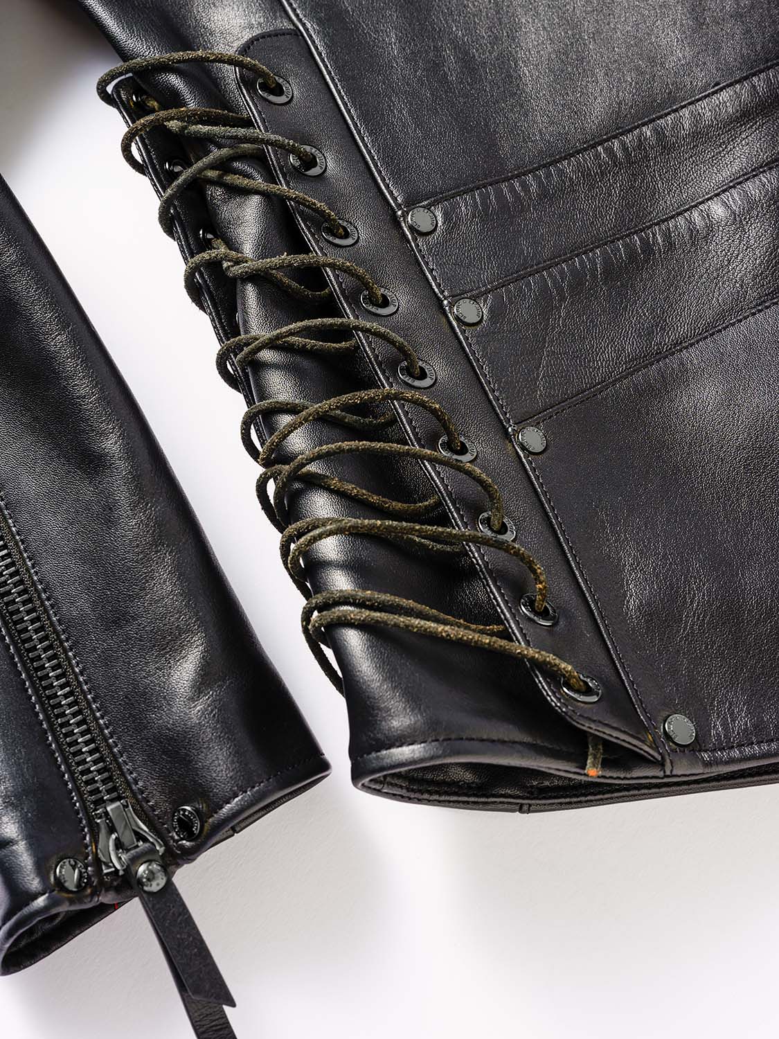 Close-up of the side of a black leather jacket featuring lace-up detailing with cord threaded through metal eyelets.