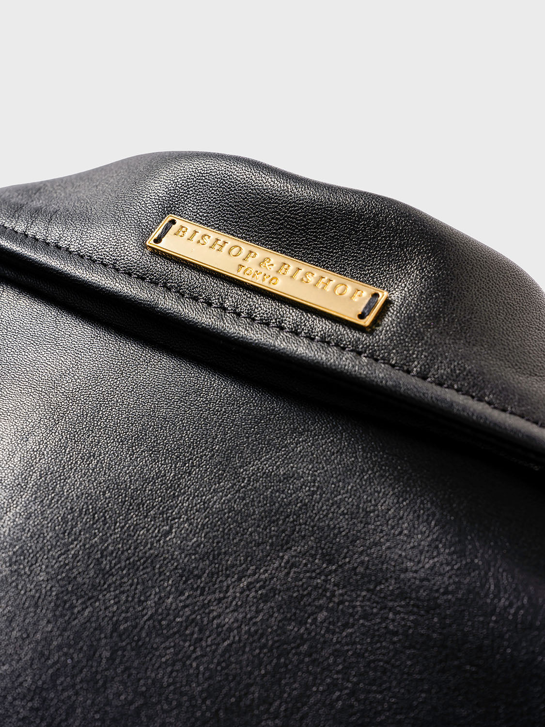 Close-up of the back of a black leather jacket collar, showing a gold plate engraved with “Bishop & Bishop Tokyo.”
