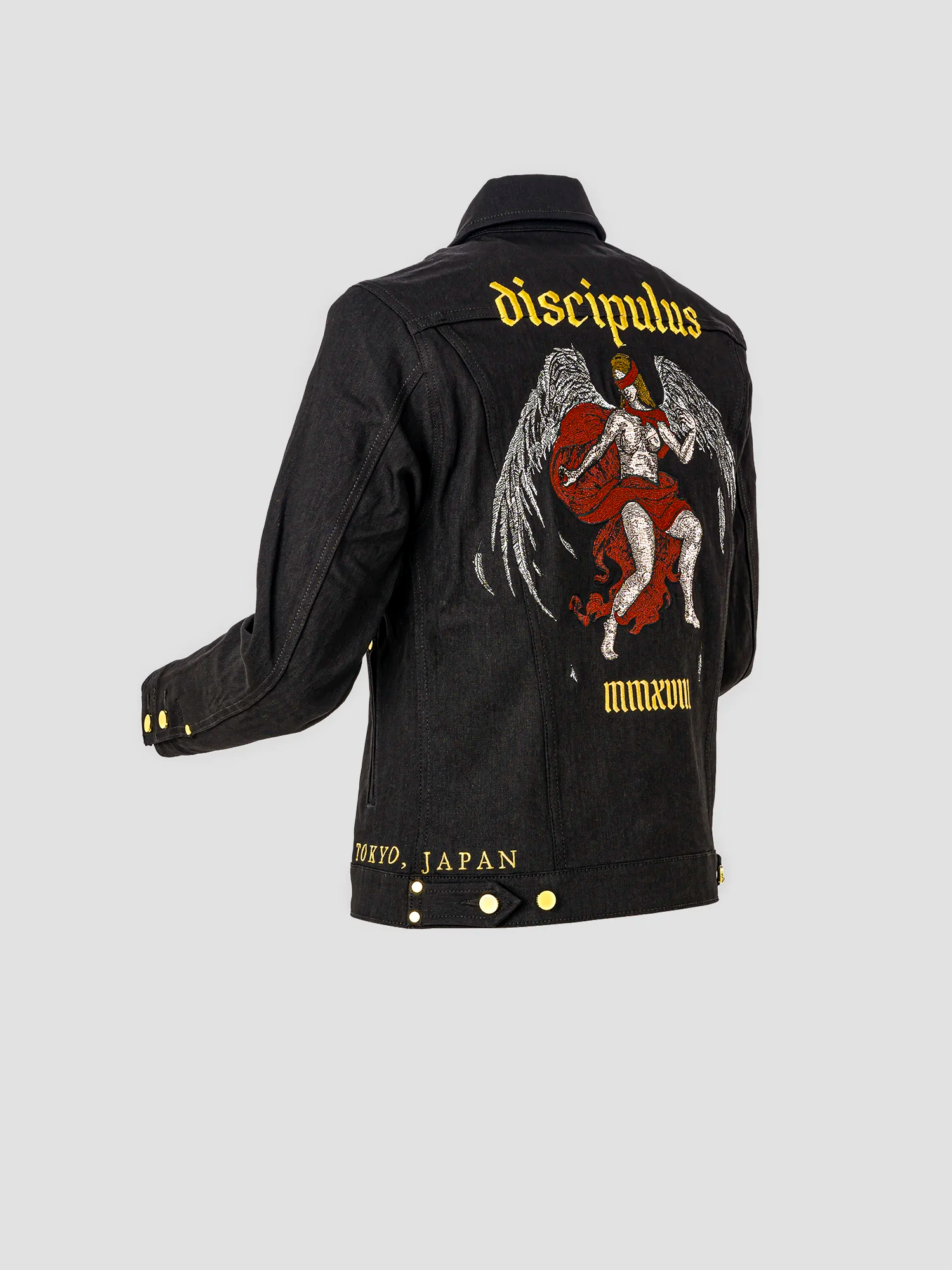 Side view of a jacket featuring an angel with wings and a red blindfold, with “DISCIPULUS” embroidered above and “MMXVIII” below.