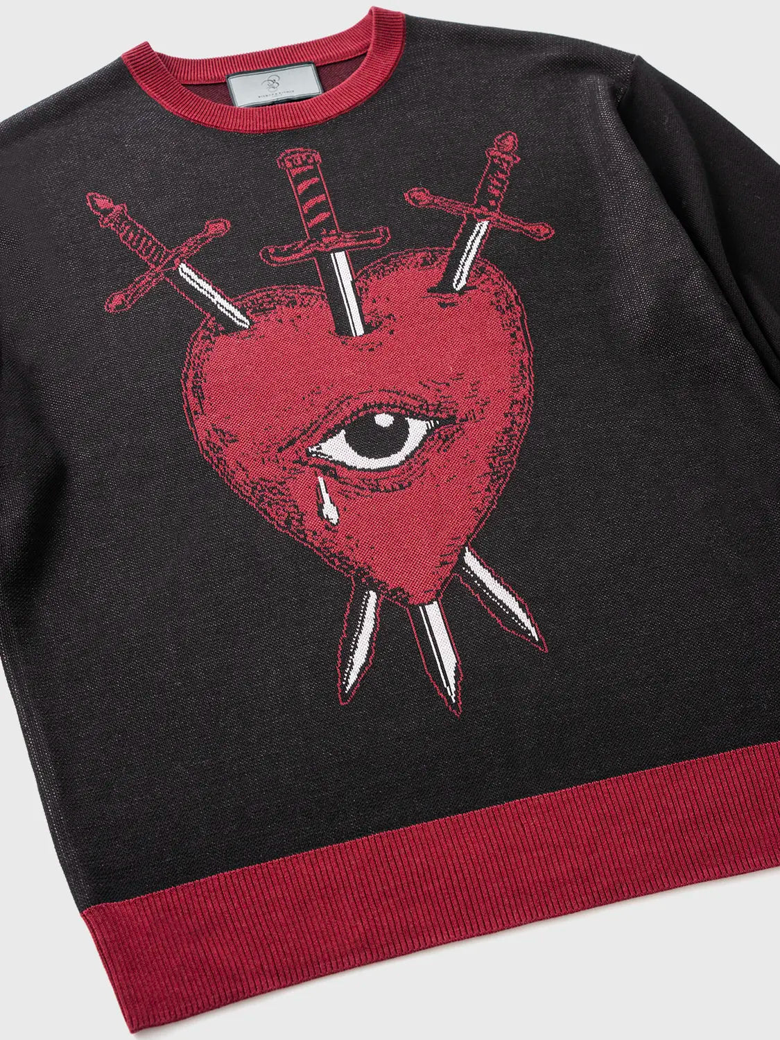 Black sweater featuring a red heart with an eye pierced by three swords graphic.