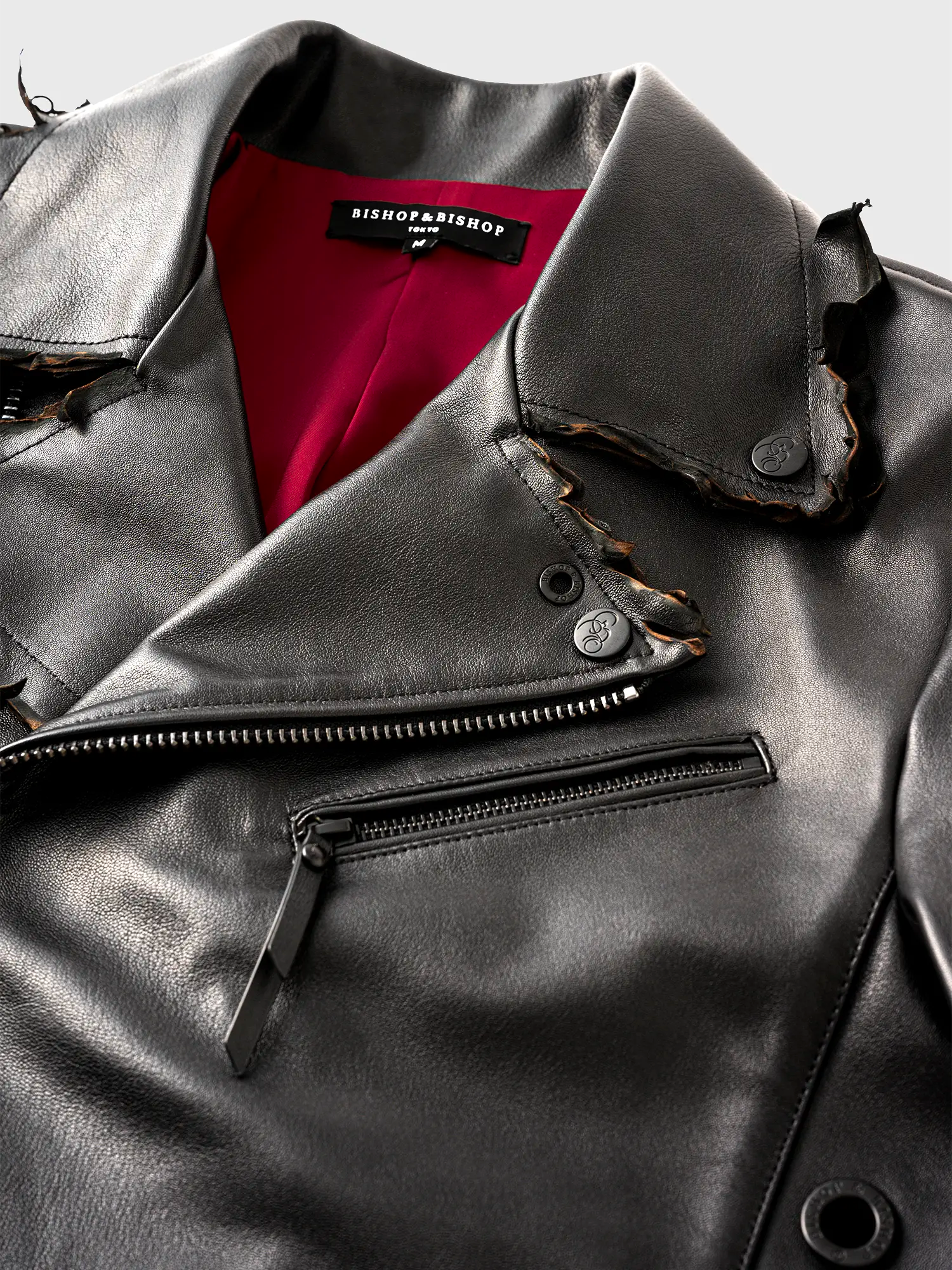 Close-up of the collar of a black leather jacket with a distressed-style design, showing red interior lining.