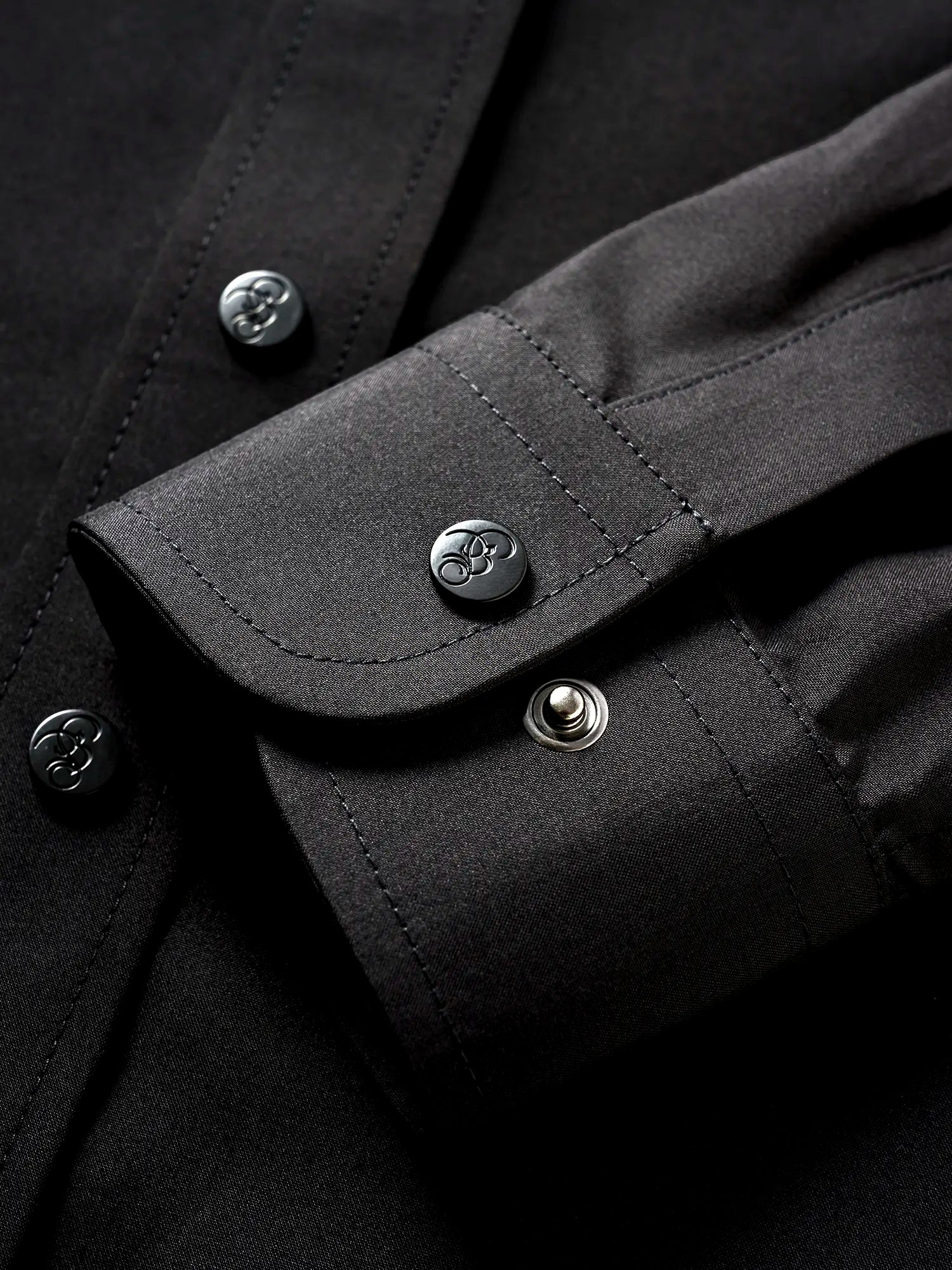 Close-up of the sleeve of a black shirt, showing buttons engraved with the Bishop & Bishop logo.