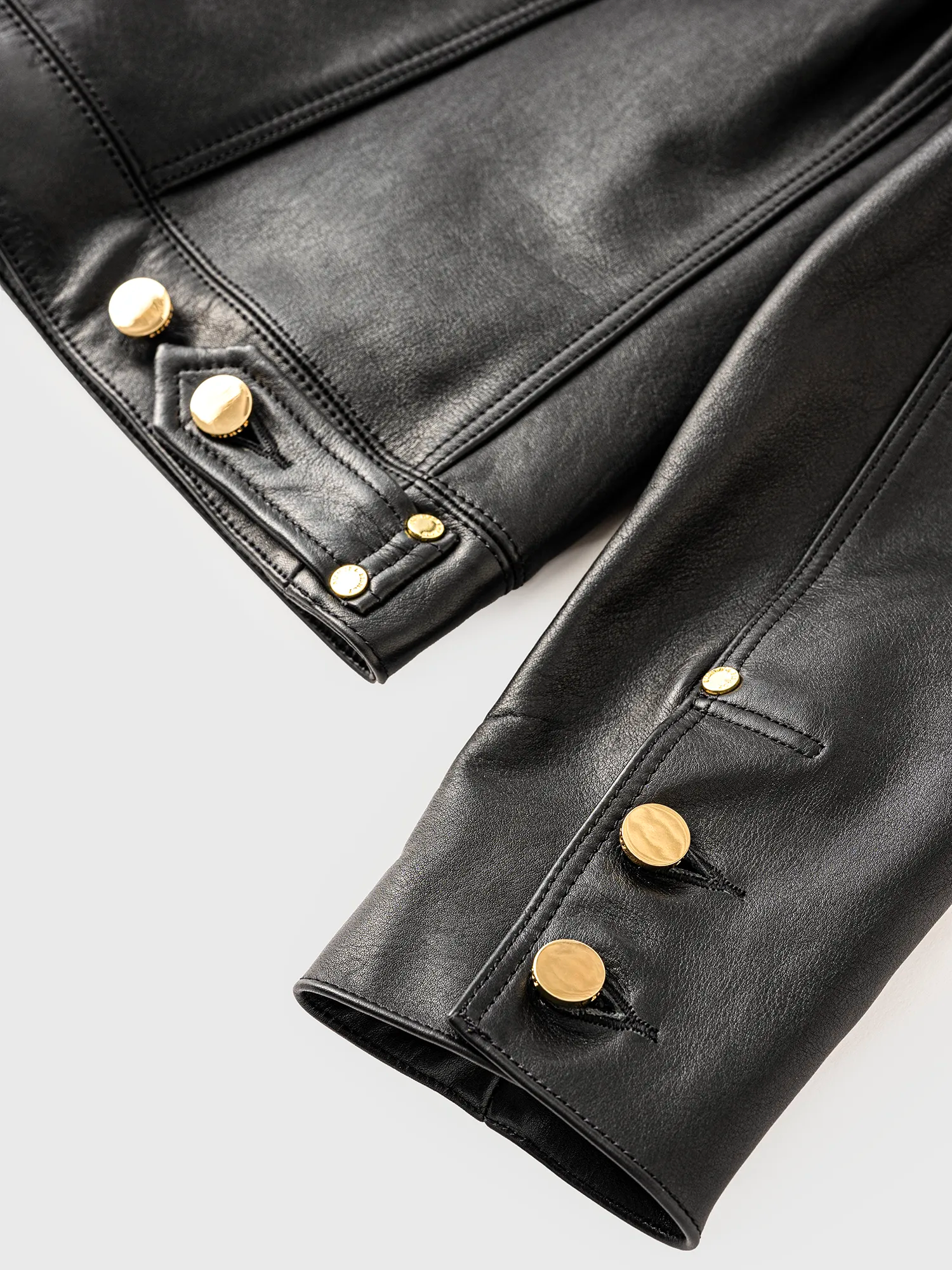 Close-up of the sleeve of a black leather jacket with gold buttons.