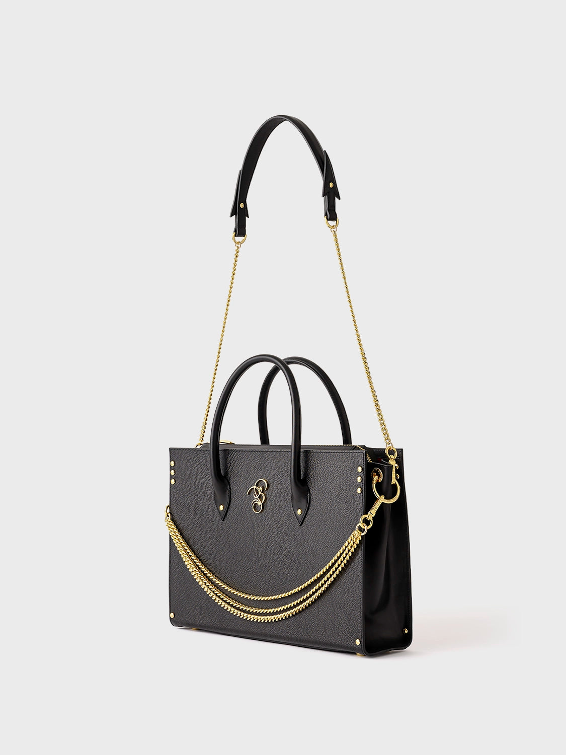 A black leather handbag with gold-toned alloy parts, featuring a detachable shoulder strap and a brand emblem on the front.