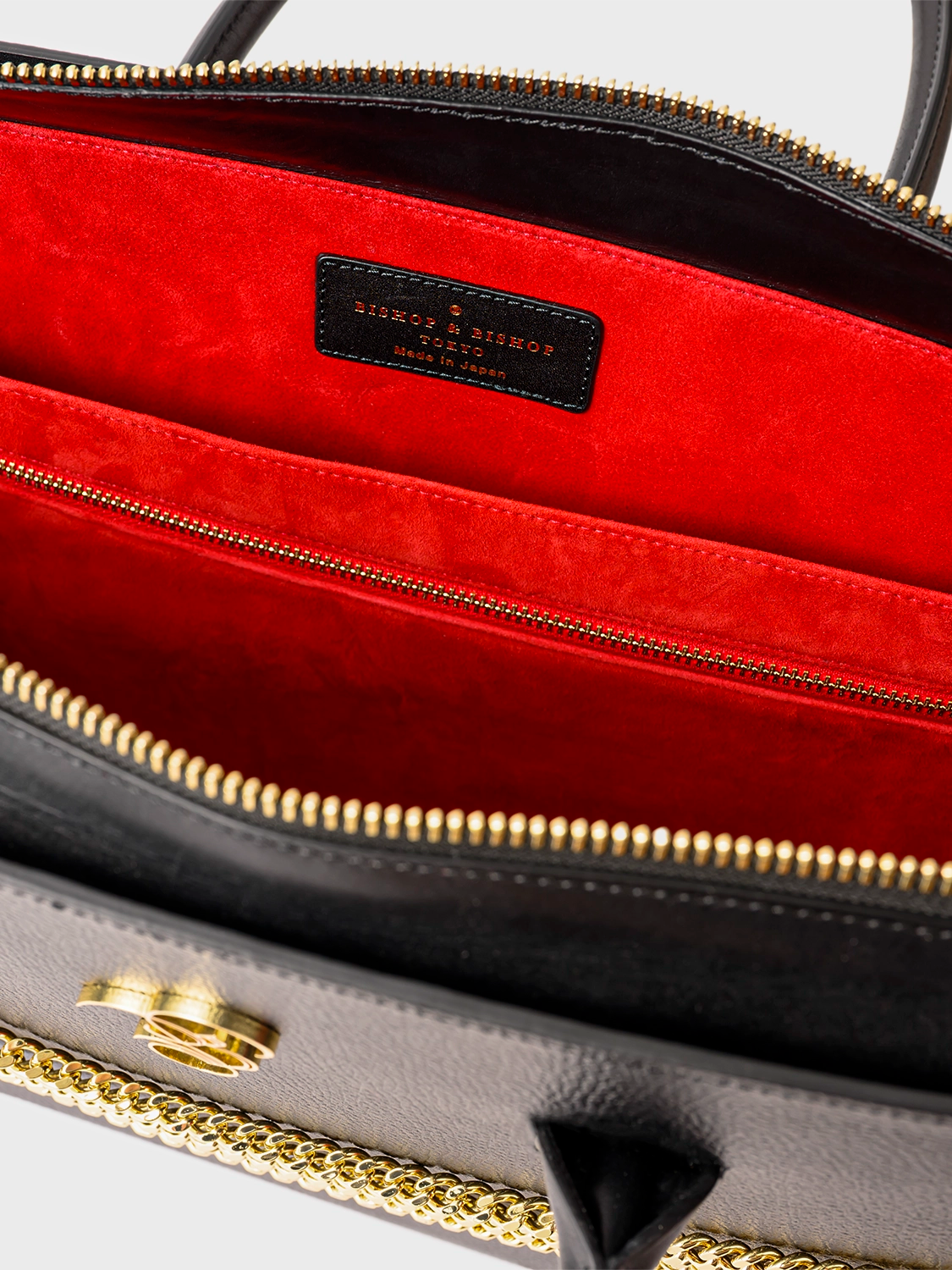 Close-up of a handbag with red interior and gold zipper, featuring a brand logo.