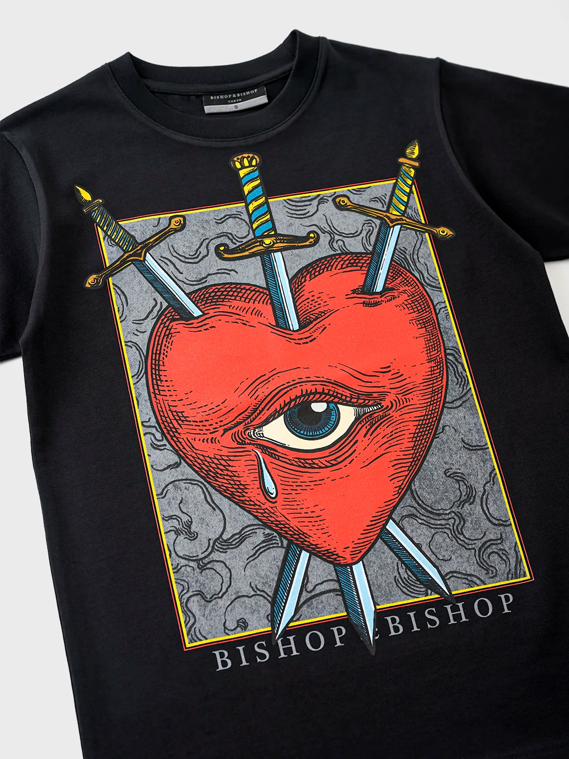 Close-up of a black crew neck t-shirt with a graphic print of a red heart, an eye, and crossed swords, and the text 'BISHOP BISHOP'.