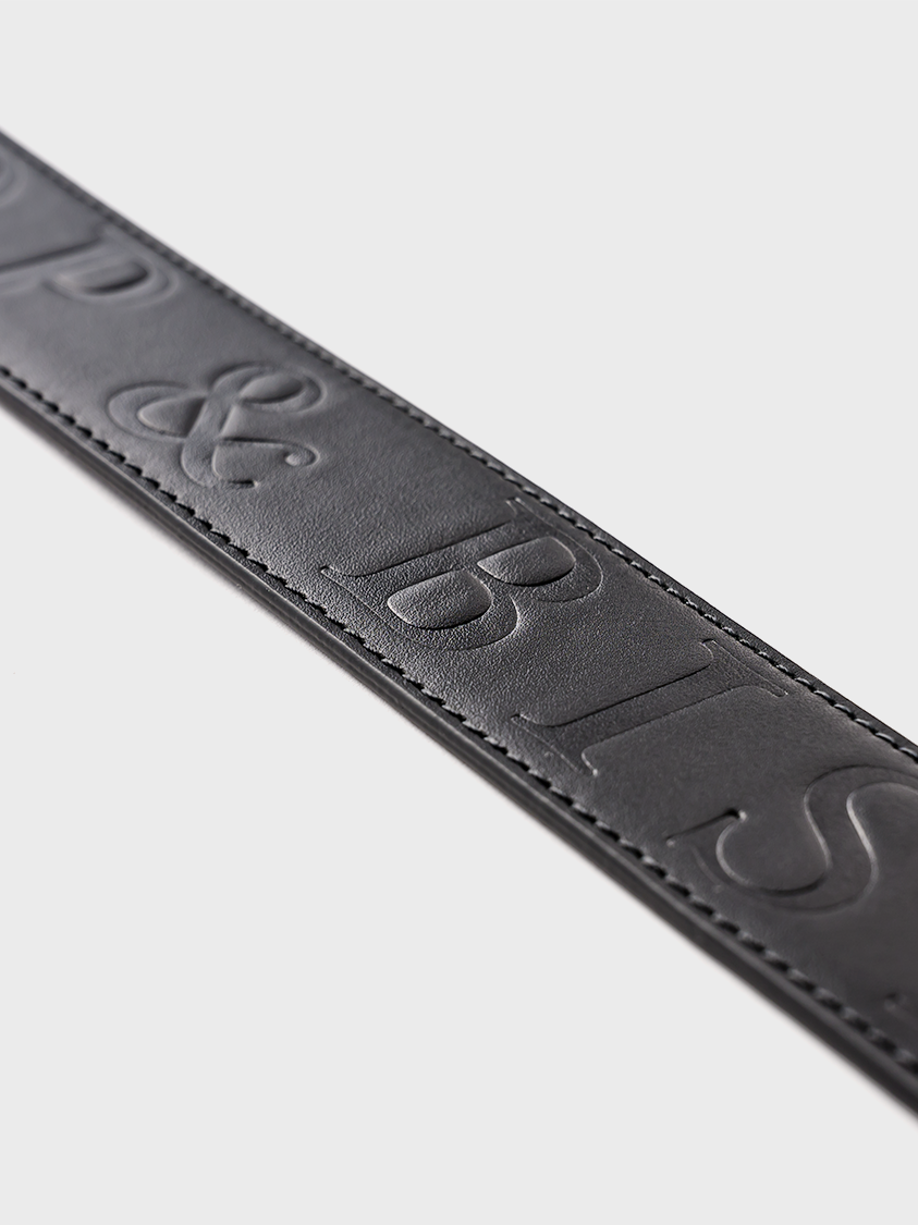 Close-up of a black leather belt showing a partial view of the embossed “Bishop & Bishop” logo.