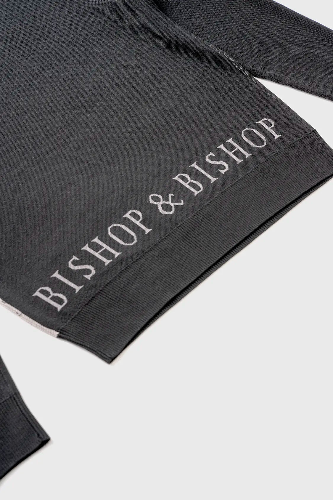 Close-up of the back of a sweater with “Bishop & Bishop” text embroidered near the bottom hem.