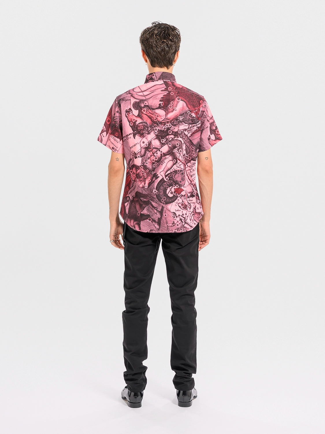 Person wearing a pink patterned shirt and black pants on a white background