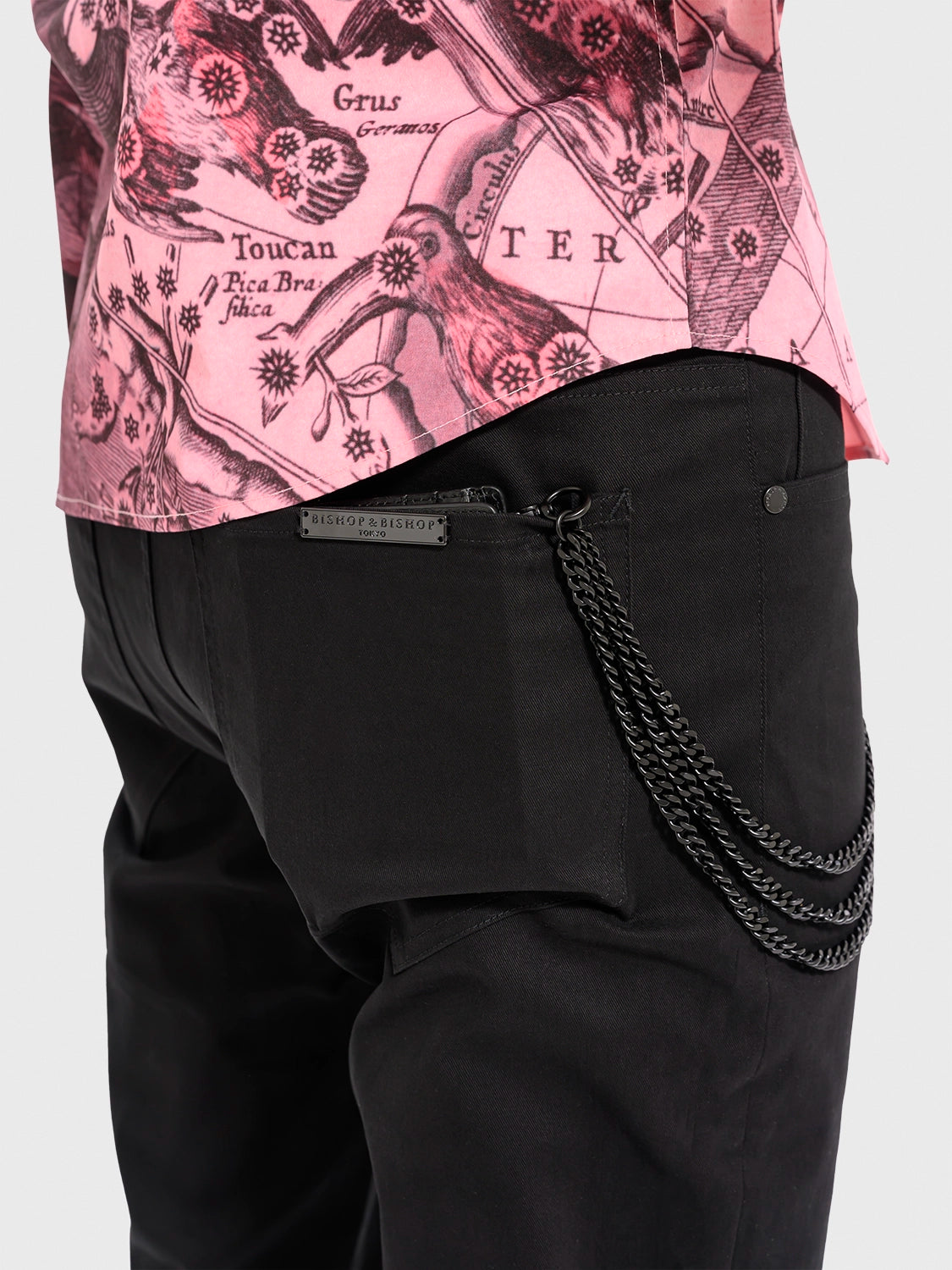 Black pants with a chain detail worn over a pink patterned top on a white background