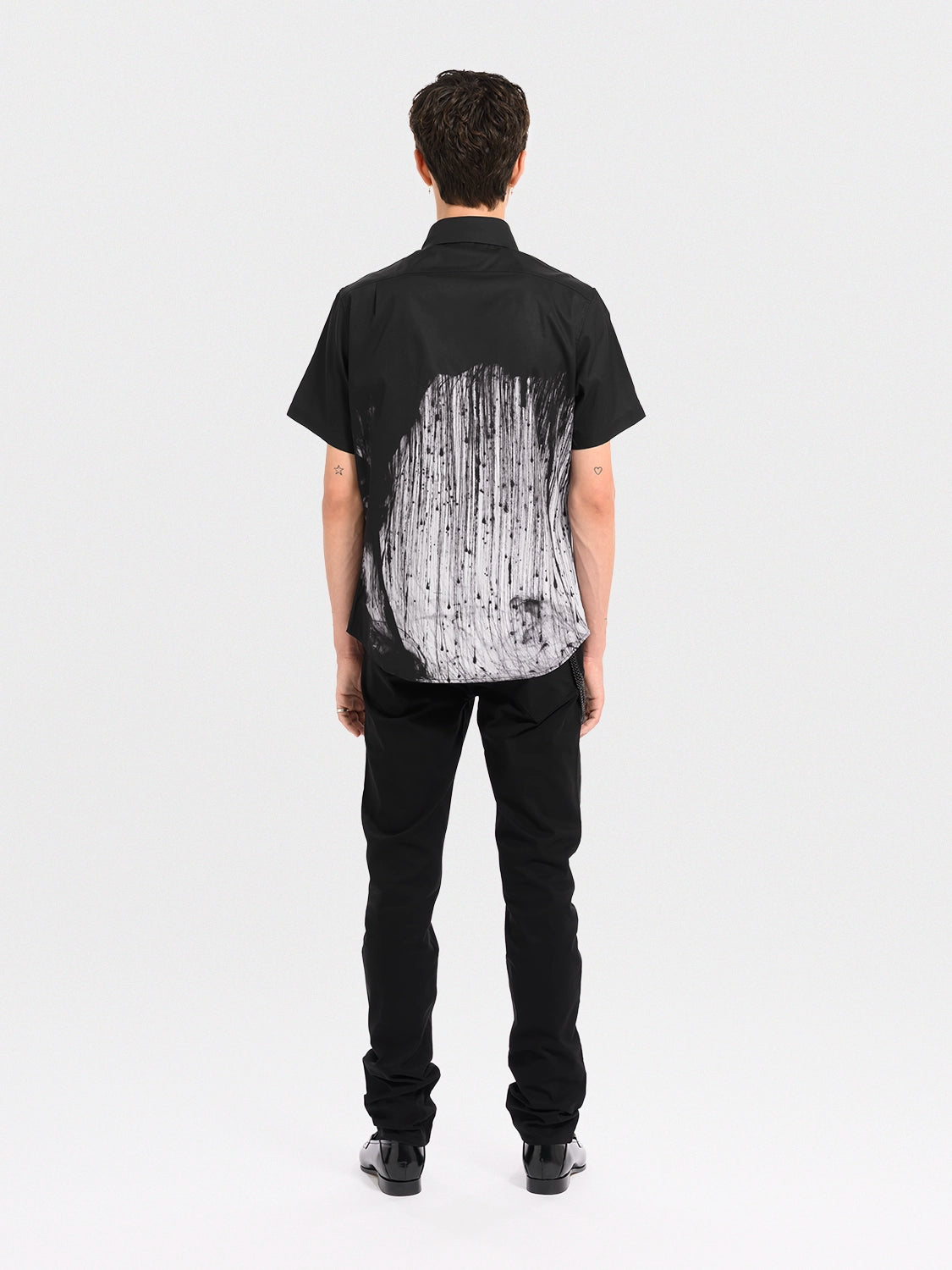 Person wearing a black shirt with a white abstract pattern on the back, standing against a white background