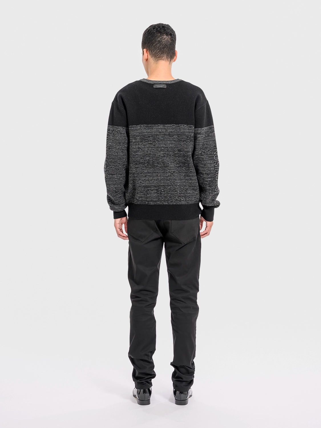 Person wearing a black and gray sweater with black pants on a white background