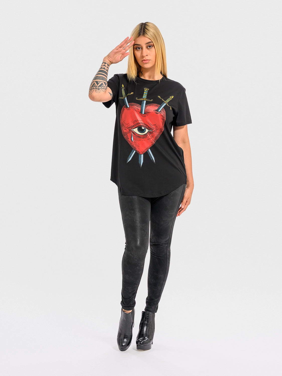 Person wearing aBlack crew neck t-shirt with a graphic print of a red heart, an eye, and crossed swords.