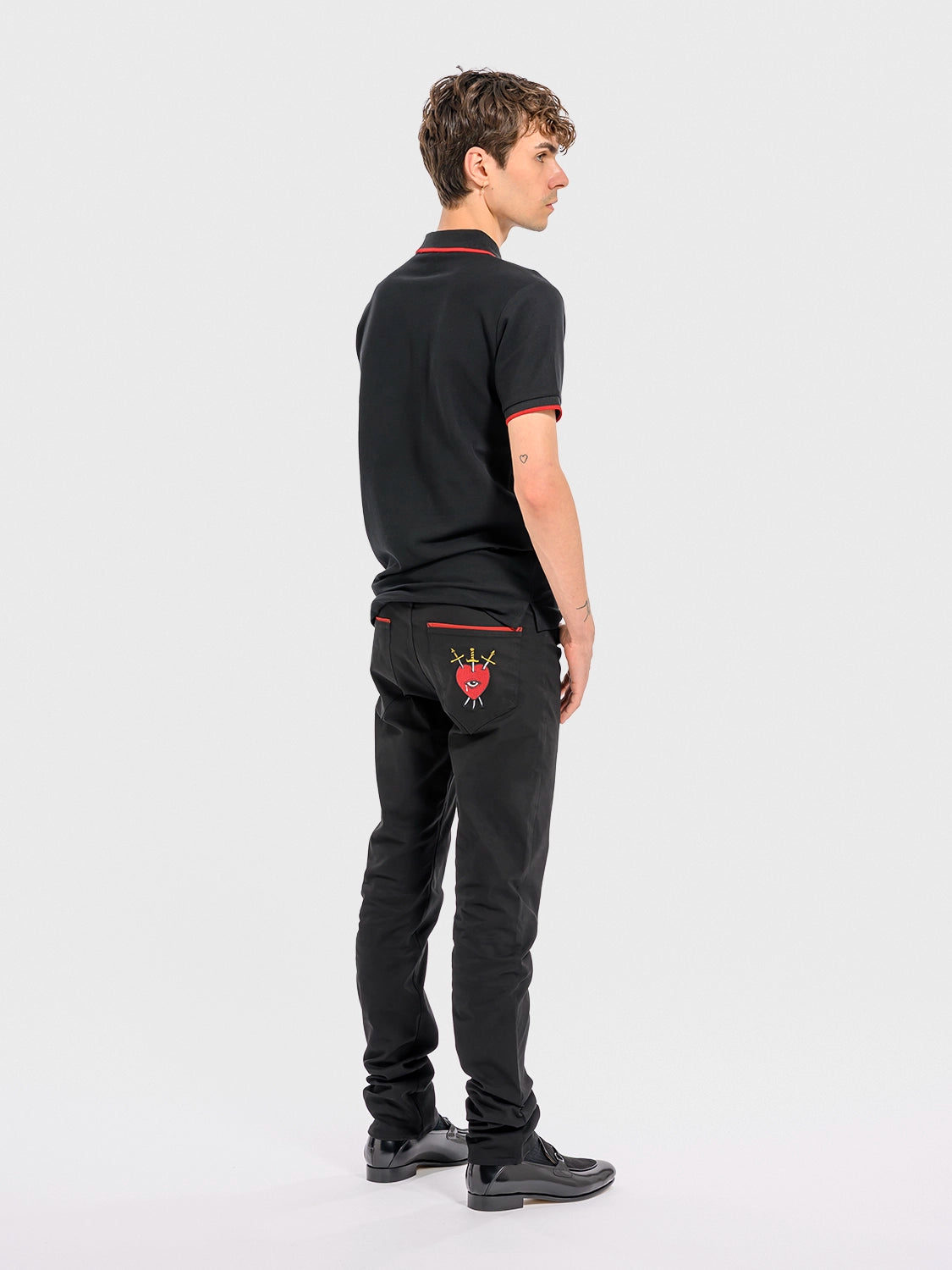Person wearing a black polo shirt and pants with red embroidery on a white background