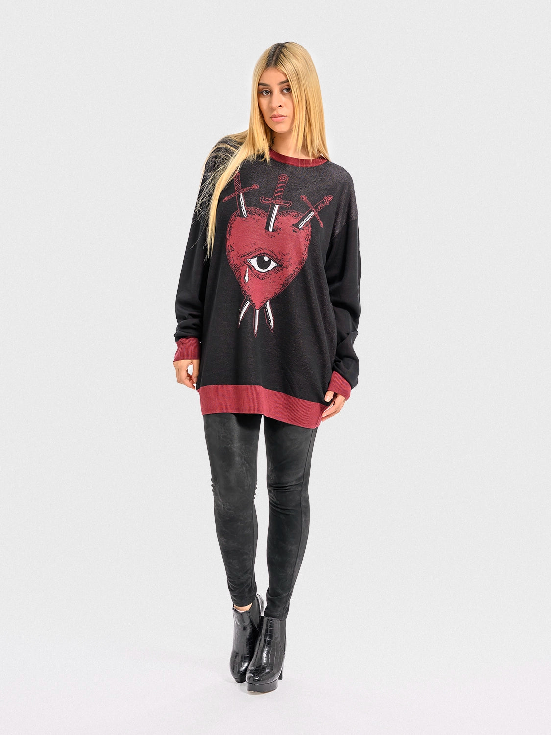 Woman wearing a black sweater with a red heart, an eye, and crossed swords, on a white background