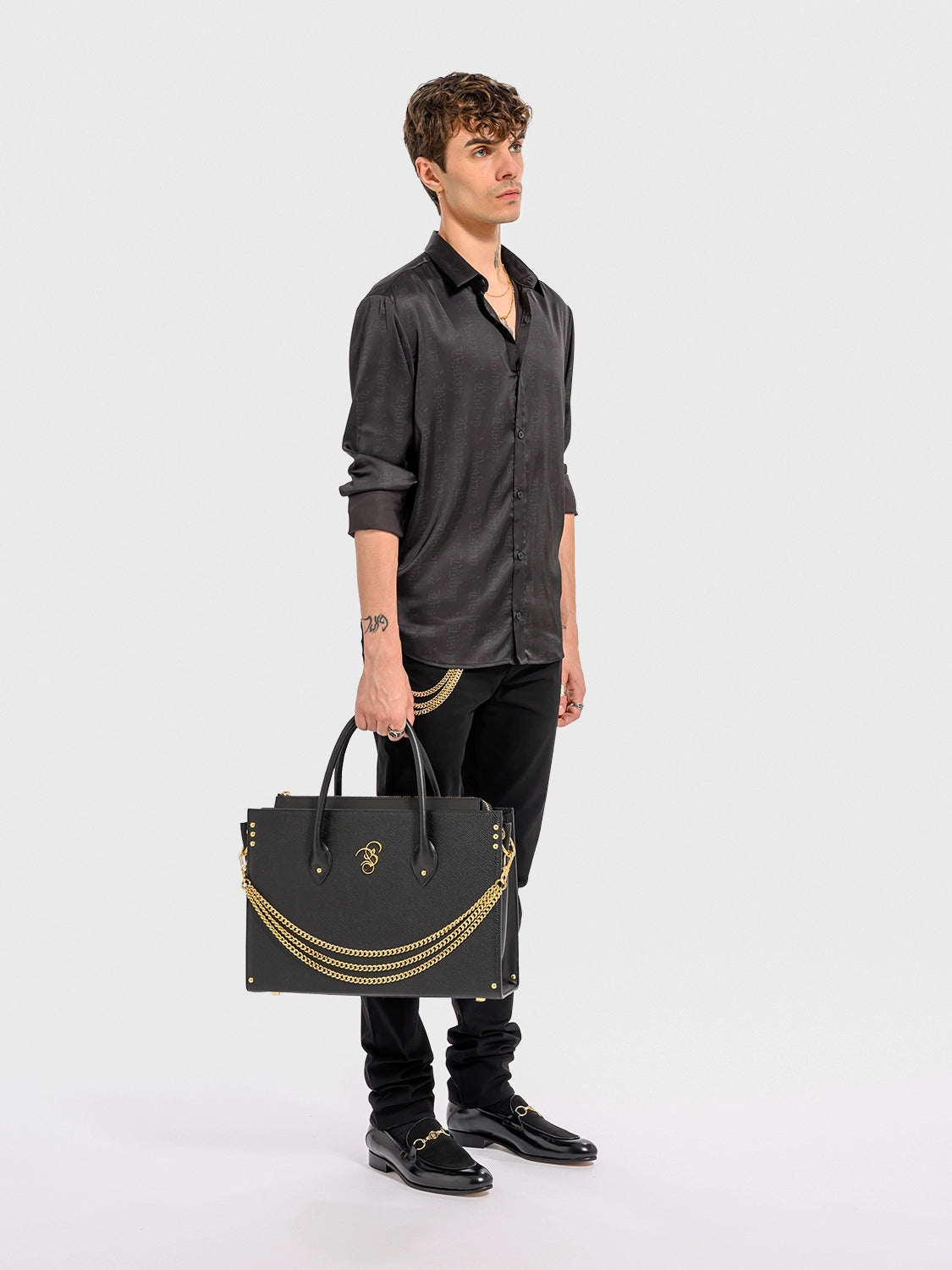 Man holding a black leather handbag with gold-toned alloy parts, featuring a detachable shoulder strap and a brand emblem on the front.