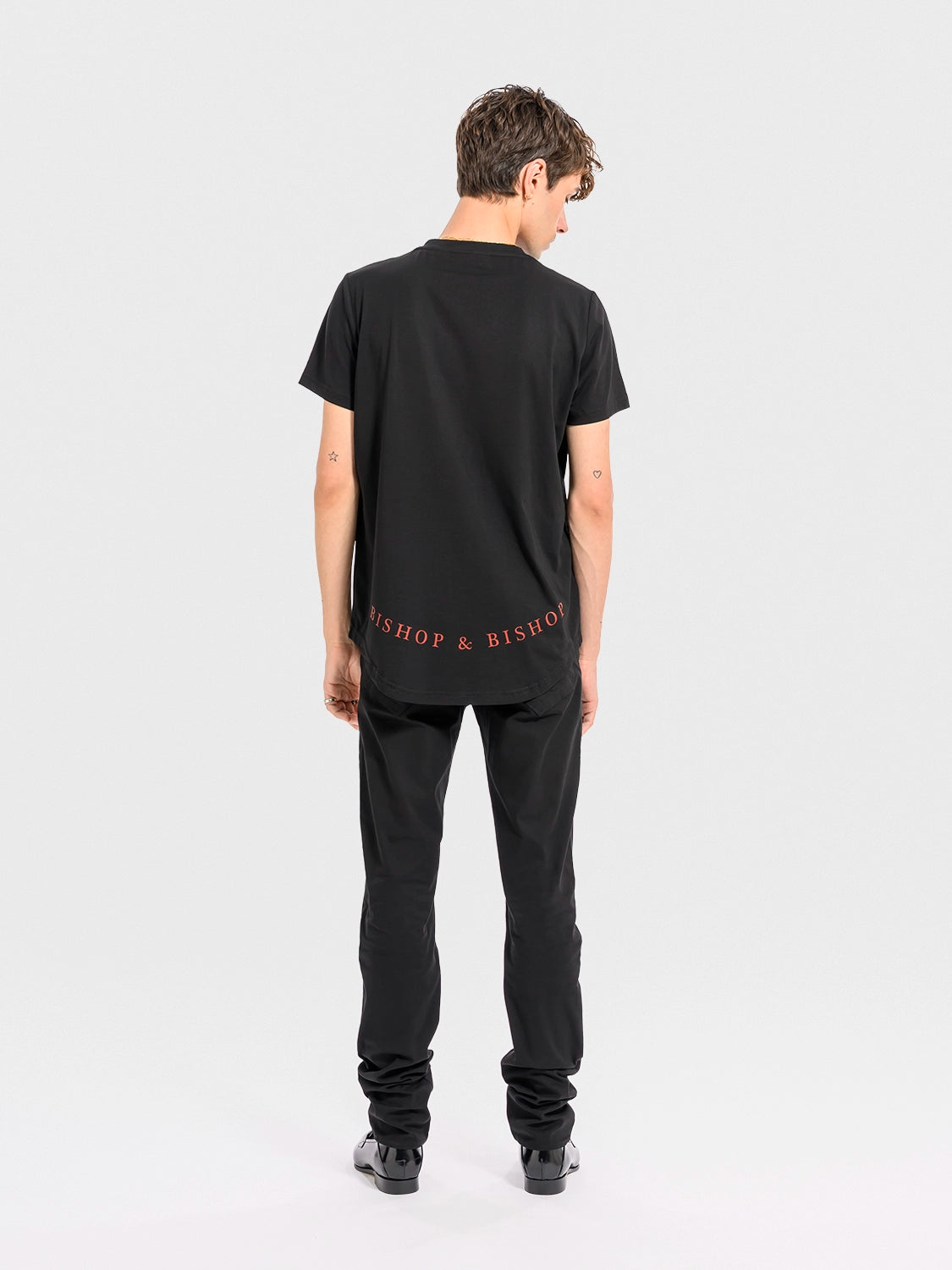 Person wearing a black t-shirt with text on the back, standing against a white background