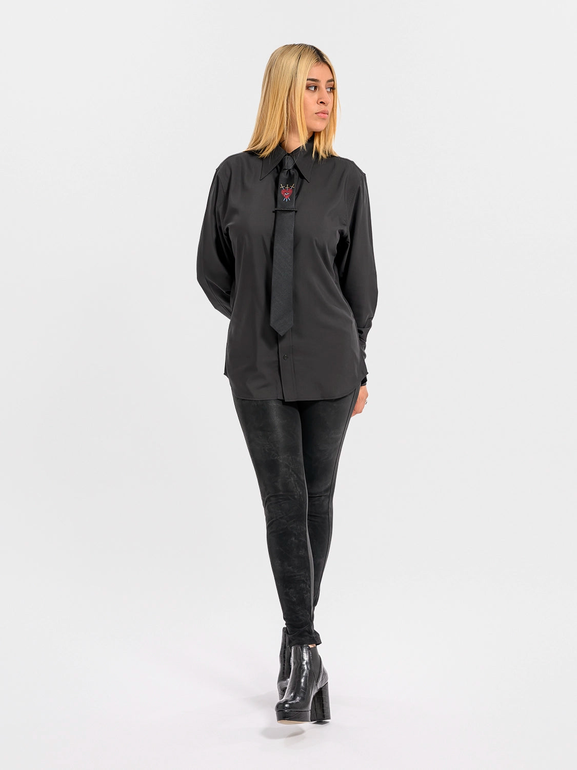 Person wearing a black shirt and black tie with a red heart, an eye, and crossed swords and black pants on a white background