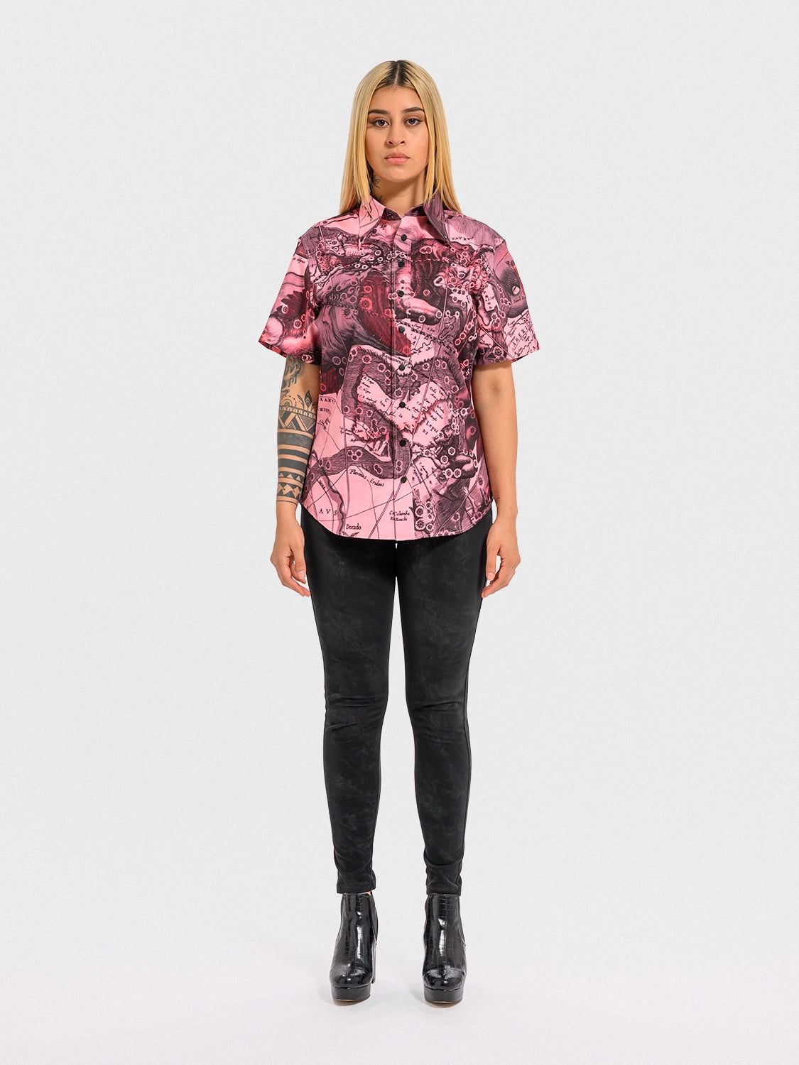 Woman wearing a pink patterned shirt and black pants on a white background