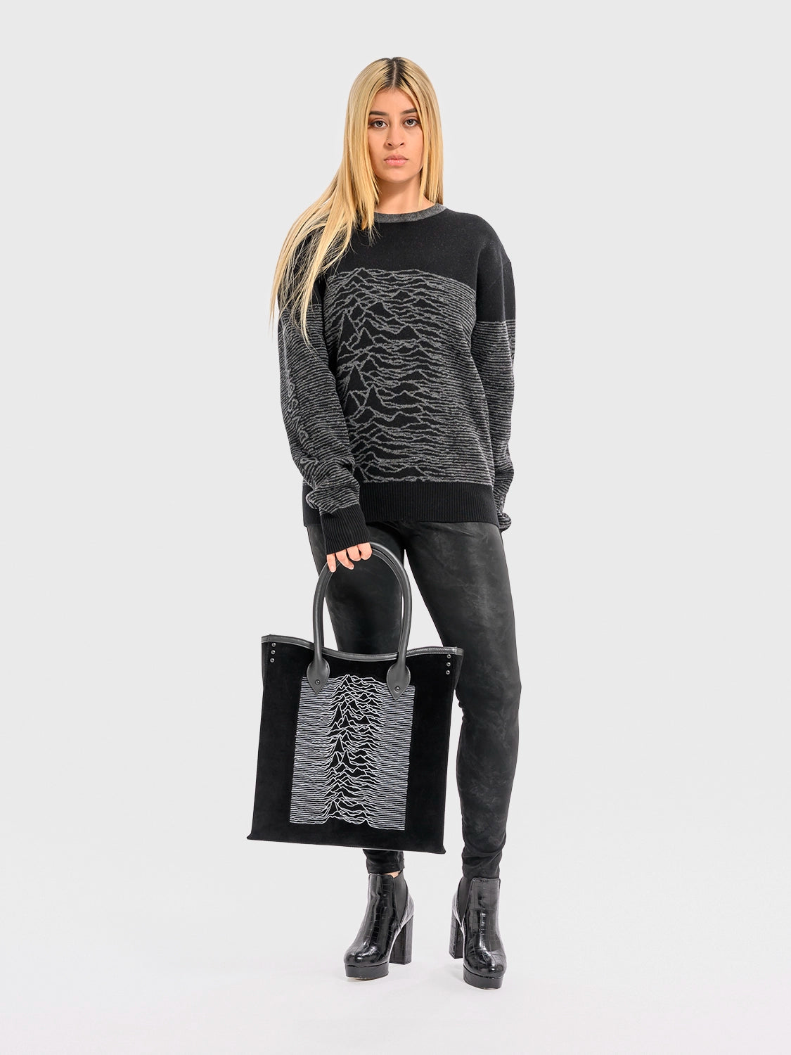 Person wearing a black and gray sweater with a matching tote bag on a white background