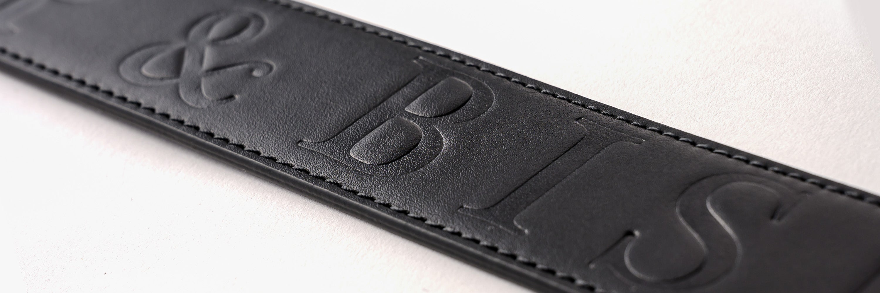 Close-up of a black belt with the embossed “Bishop & Bishop” logo, displayed on a gray background.