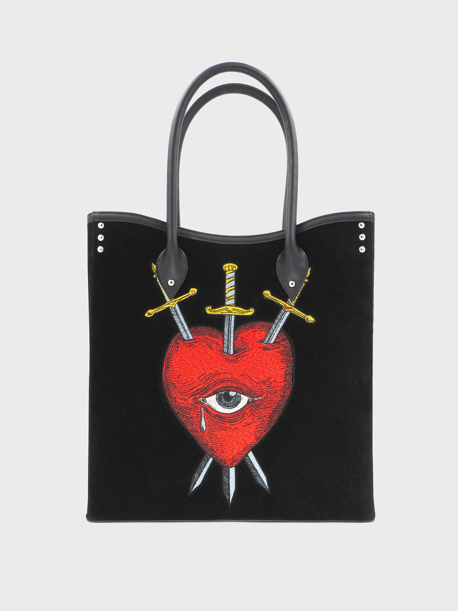 Black velvet and leather tote bag with a red heart, an eye, and crossed swords embroidered on the front, with a black handle.