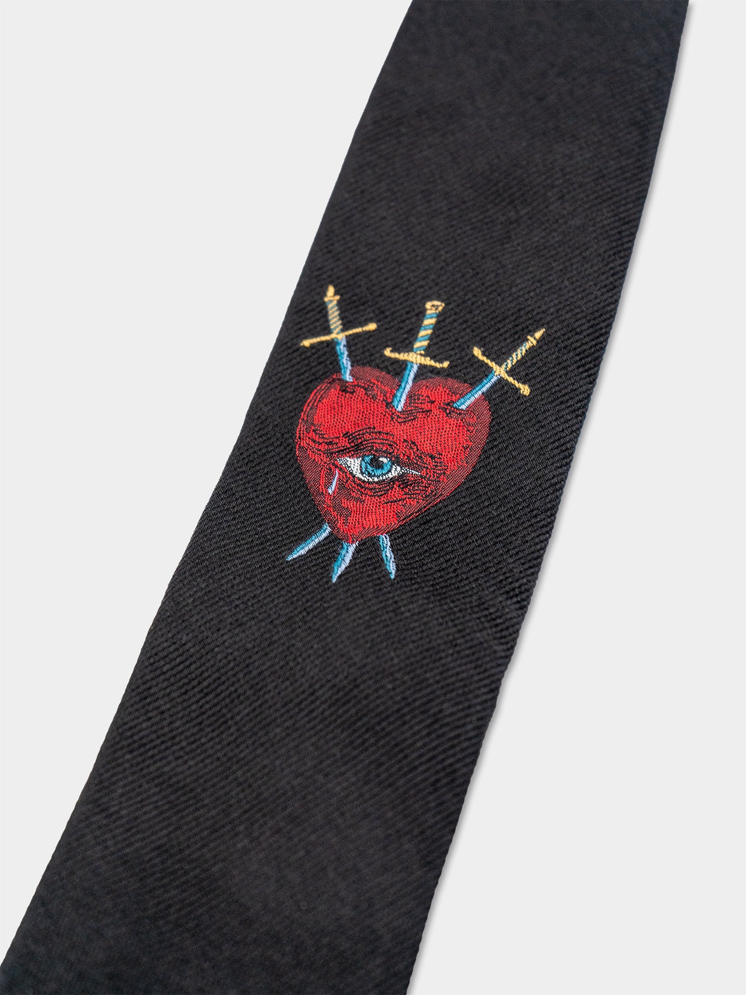 Close-up of a black tie with a red heart, an eye, and crossed swords design