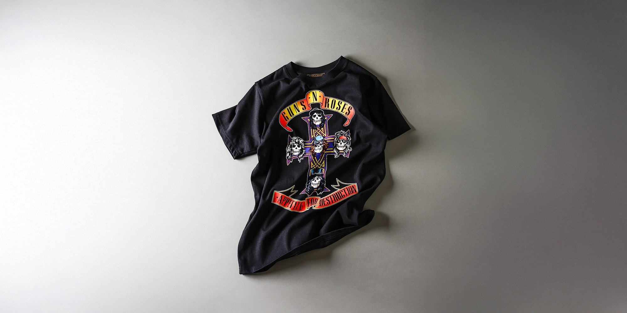 Black Guns N’ Roses T-shirt featuring a cross with five skulls and the text “Appetite for Destruction” beneath, displayed on a gray background.
Black Guns N’ Roses T-shirt featuring a cross with five skulls and the text “Appetite for Destruction” beneath, displayed on a gray background.