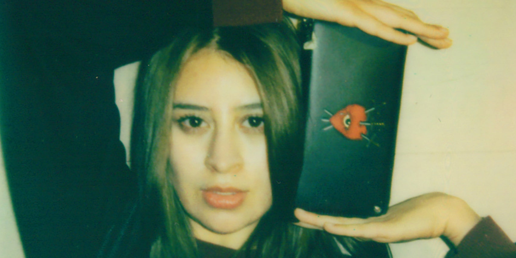 Close-up of a woman’s face holding a black wallet featuring a red heart with an eye pierced by three swords graphic.