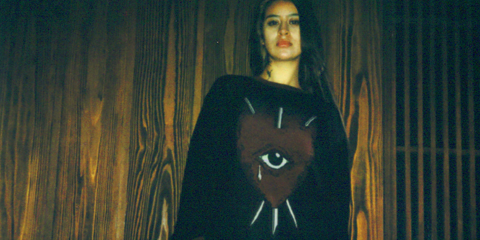 Woman wearing a black sweater featuring a red heart with an eye pierced by three swords graphic