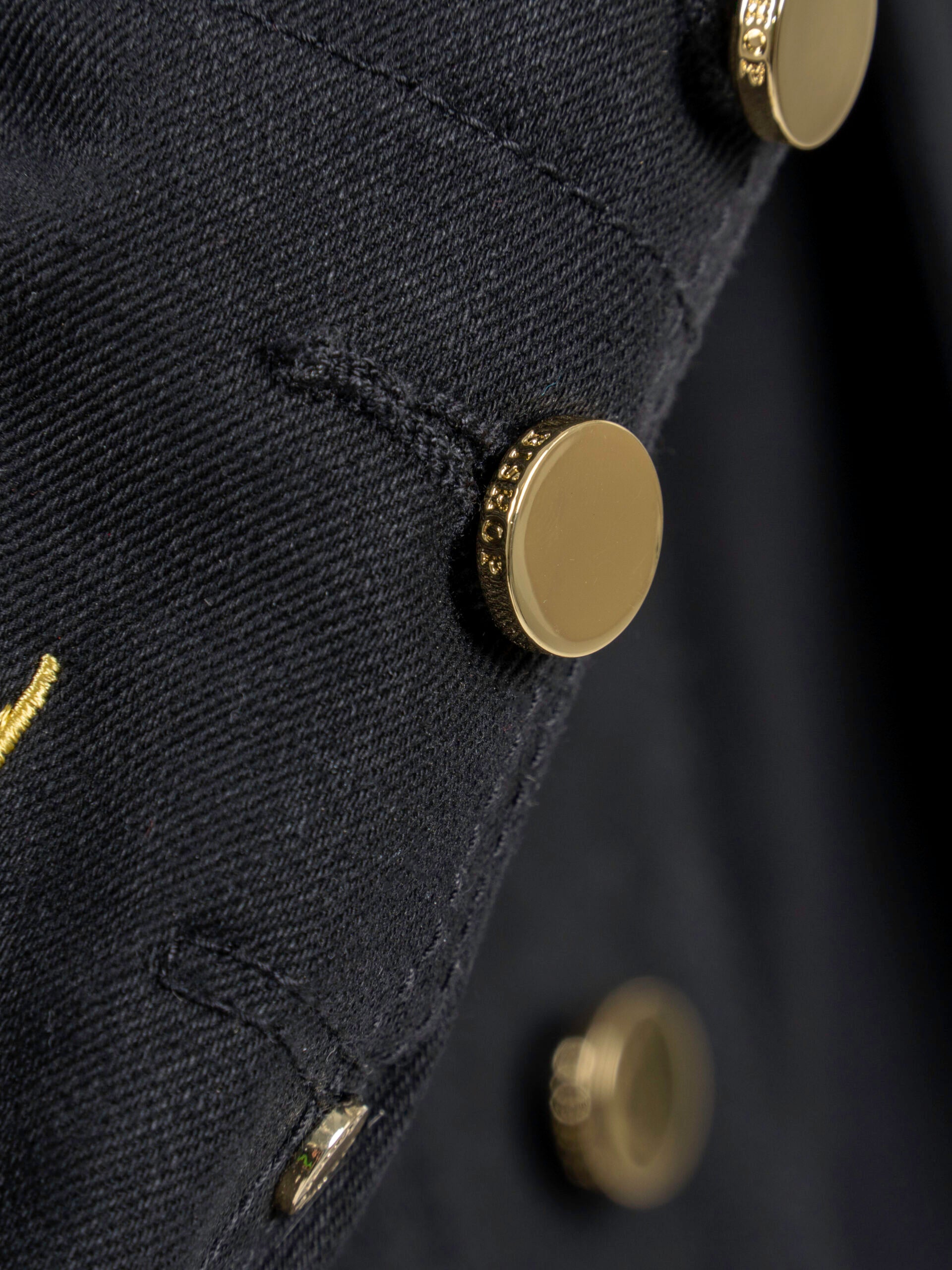 Close-up of the sleeve of a black jacket with gold buttons.