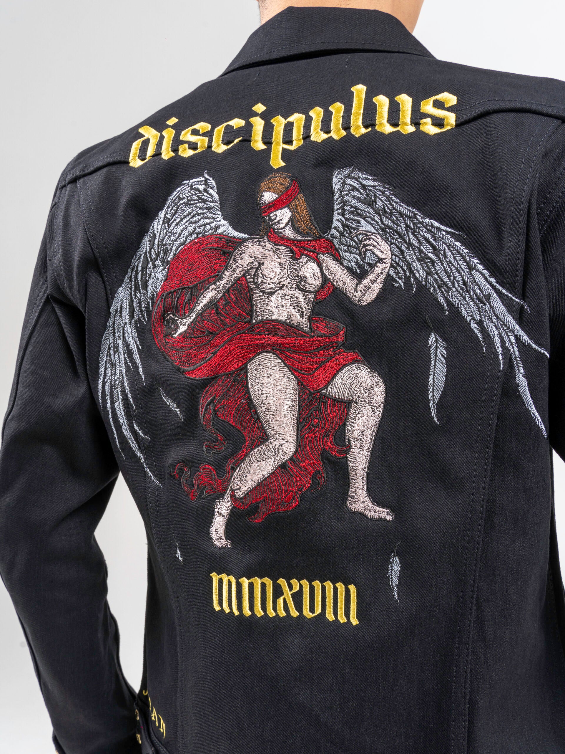 Rear view of a jacket featuring an angel with wings and a red blindfold, with “DISCIPULUS” embroidered above and “MMXVIII” below.