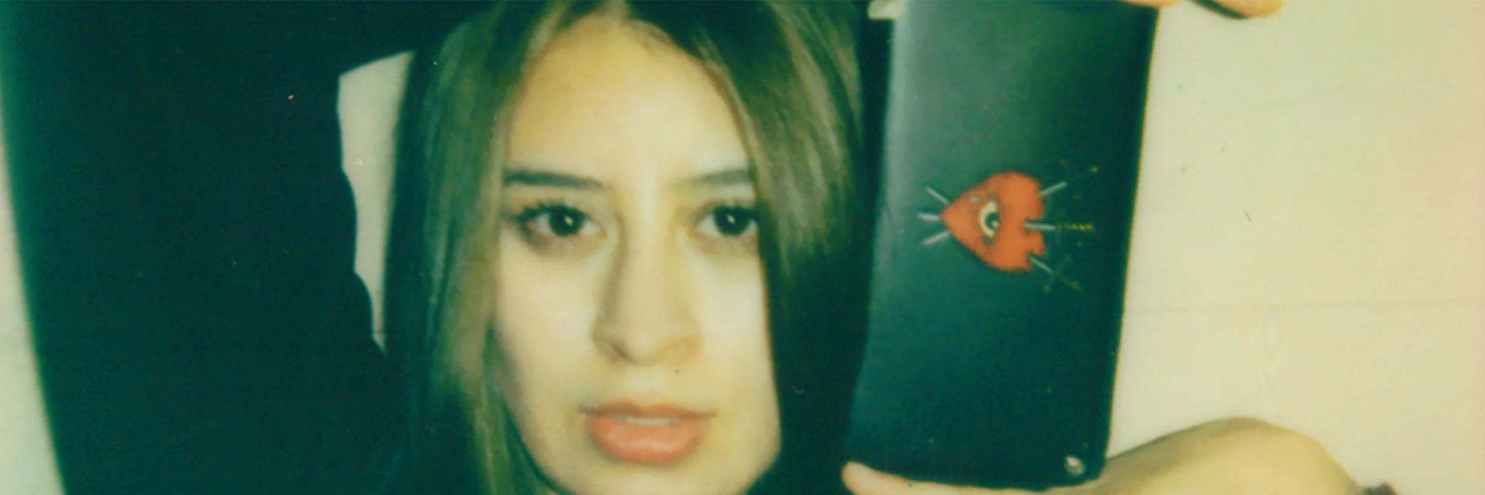 Close-up of a woman’s face holding a black wallet featuring a red heart with an eye pierced by three swords graphic.