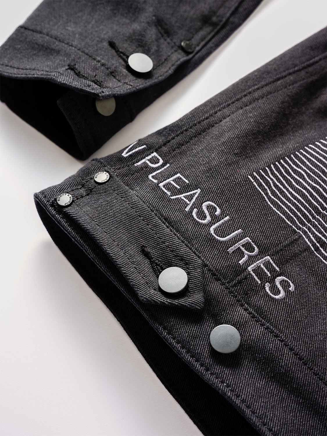 Close-up of the cuff with “UNKNOWN PLEASURES” embroidery and matte buttons.