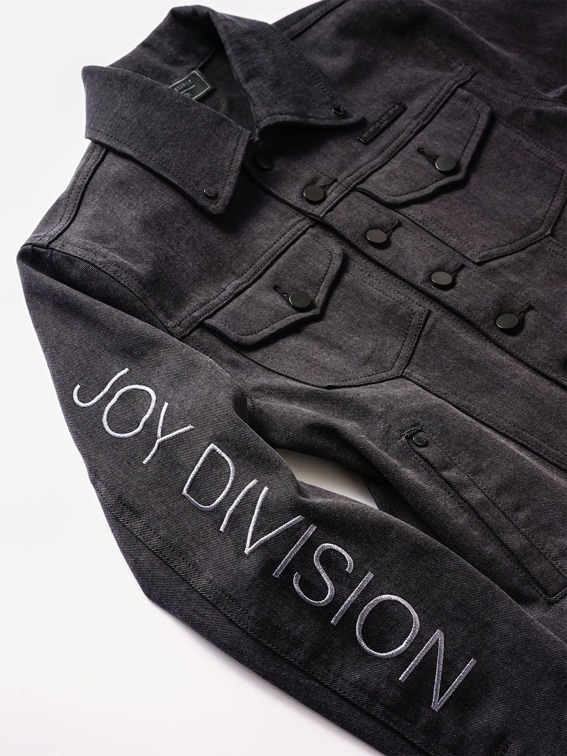 Side view close-up of the embossed JOY DIVISION text along the sleeve seam.