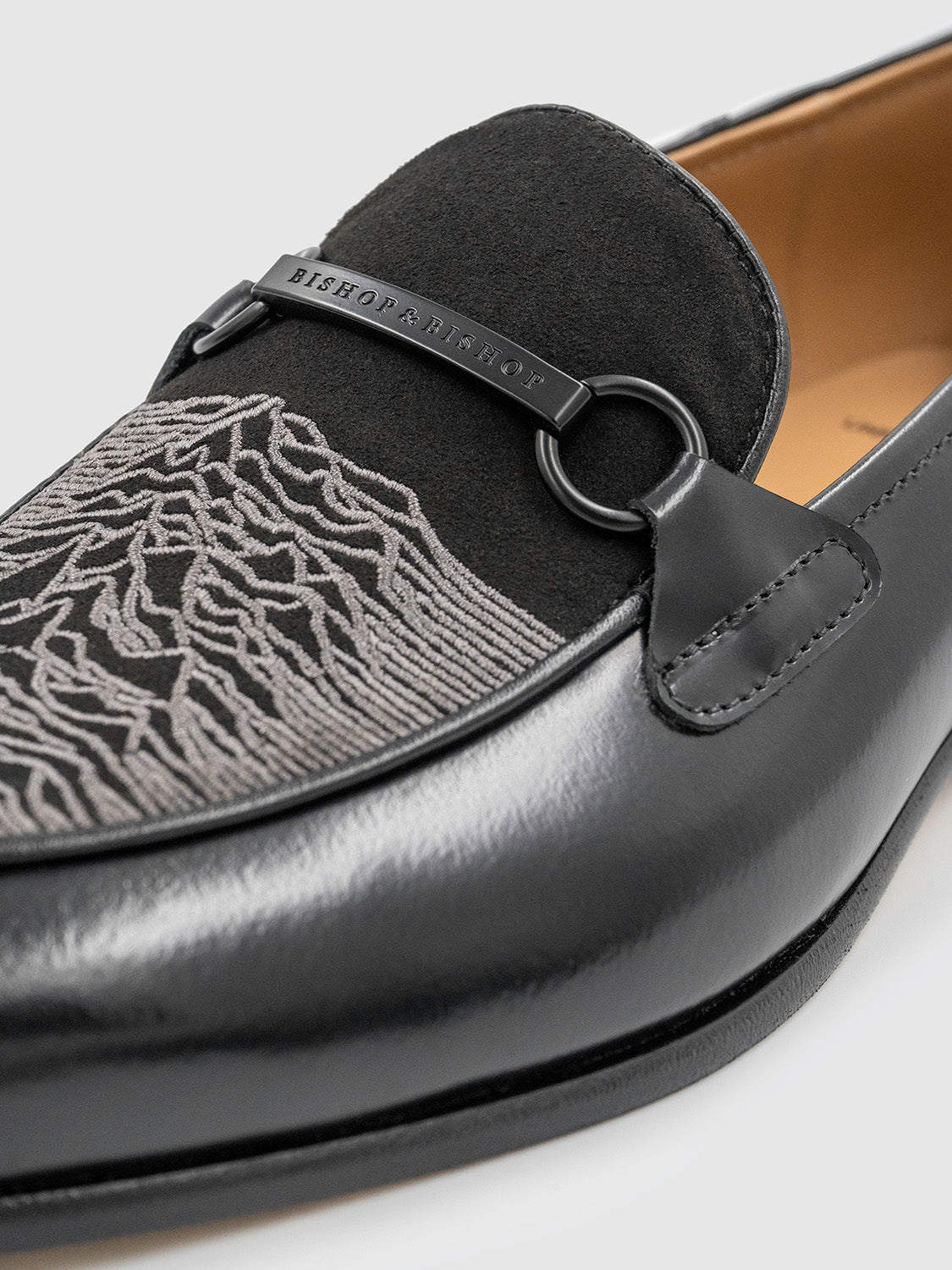 Close-up of the suede tongue embroidered with the Unknown Pleasures waveform in charcoal grey.
