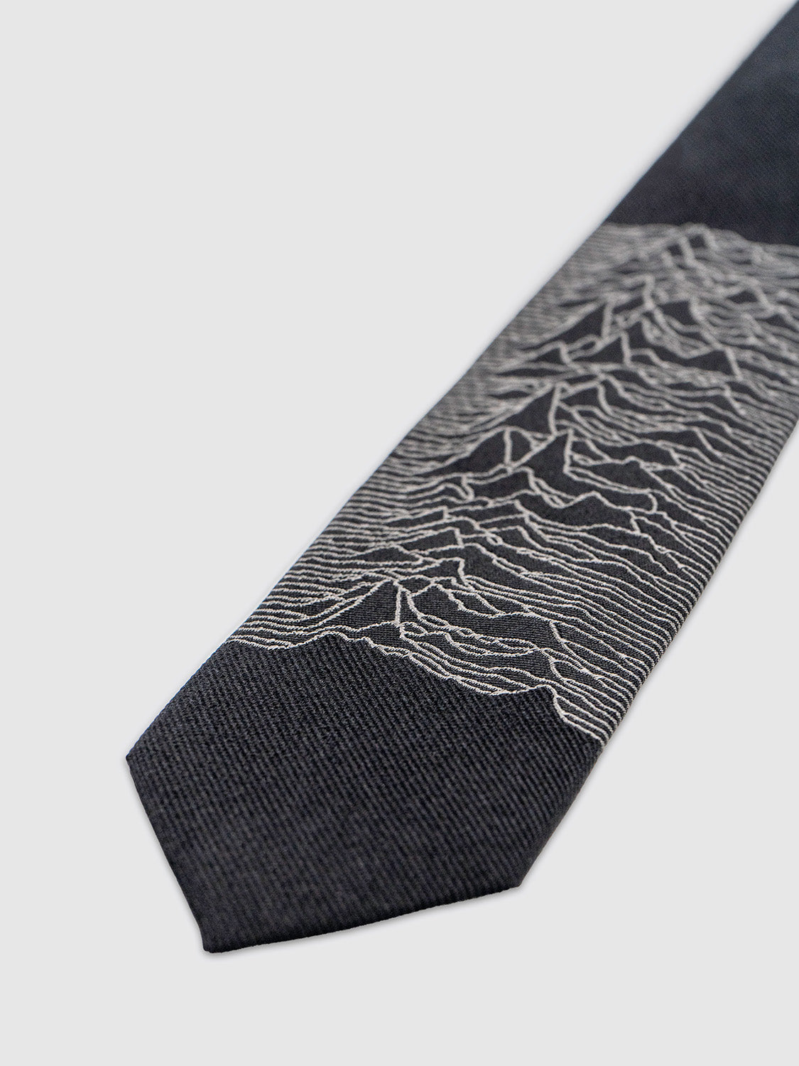Close-up of the lower half of the tie showcasing the finely woven Unknown Pleasures waveform in grey jacquard.
