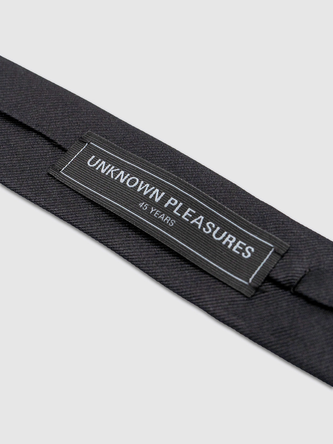Close-up of the tie’s branded label stitched on the back side in tonal black-on-black thread.