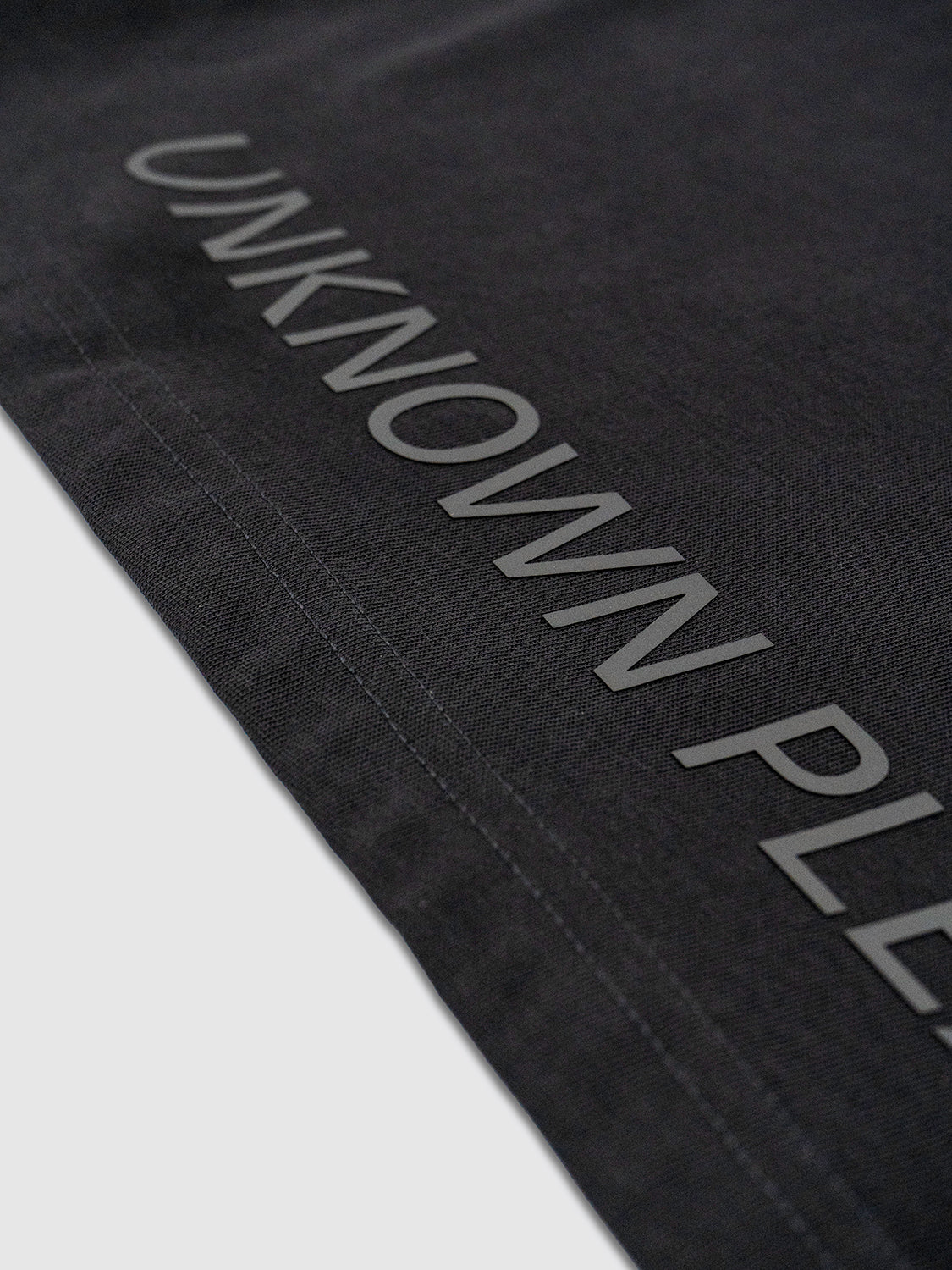 Close-up of the hem label featuring UNKNOWN PLEASURES in tonal silicone lettering.