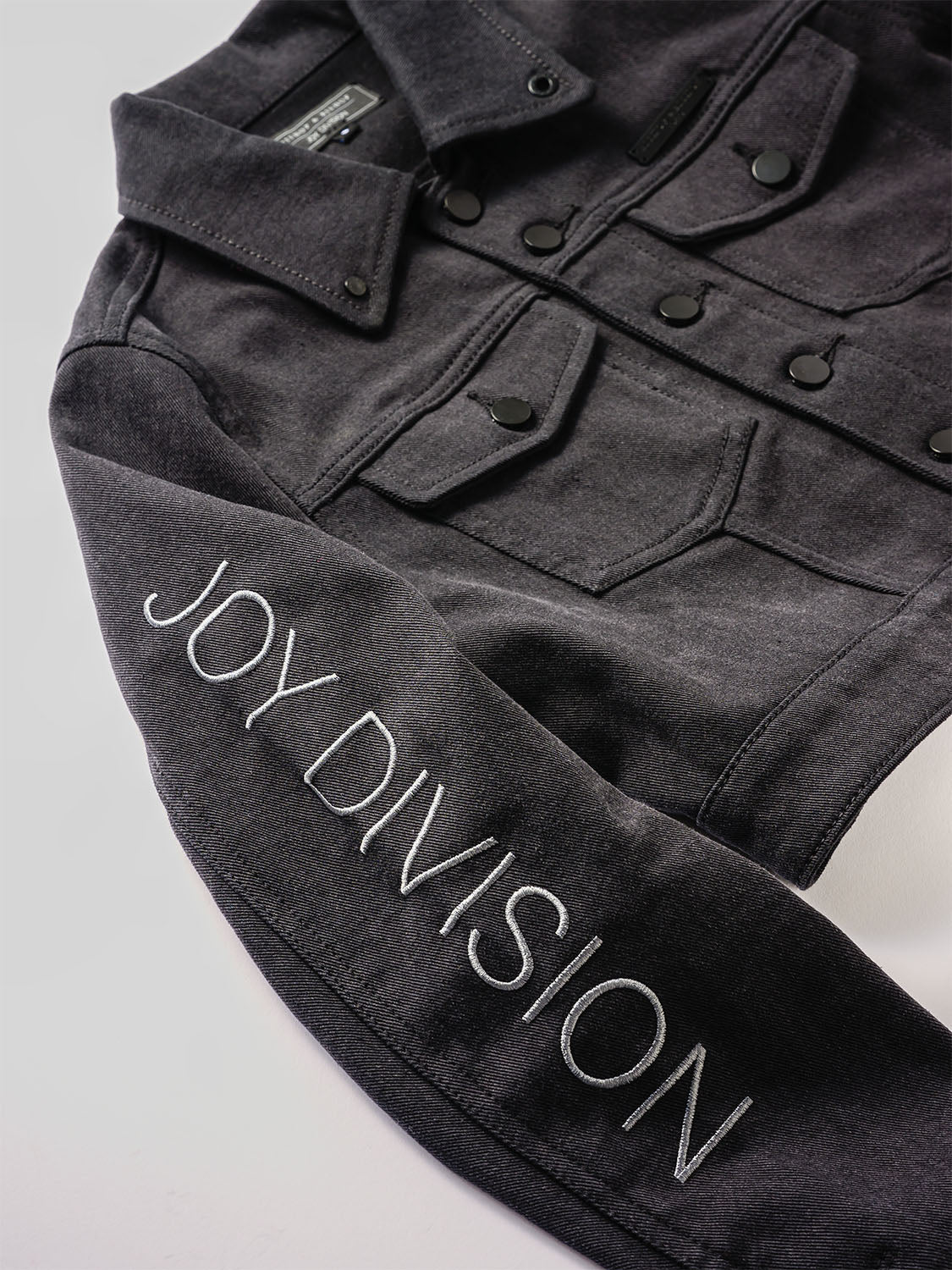 Close-up of the sleeve with JOY DIVISION embroidery and tonal snap buttons.